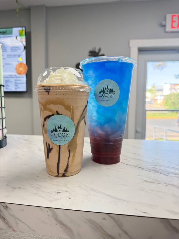 A caramel and chocolate drizzled protein shake with whipped cream next to a blue and purple layered energy tea